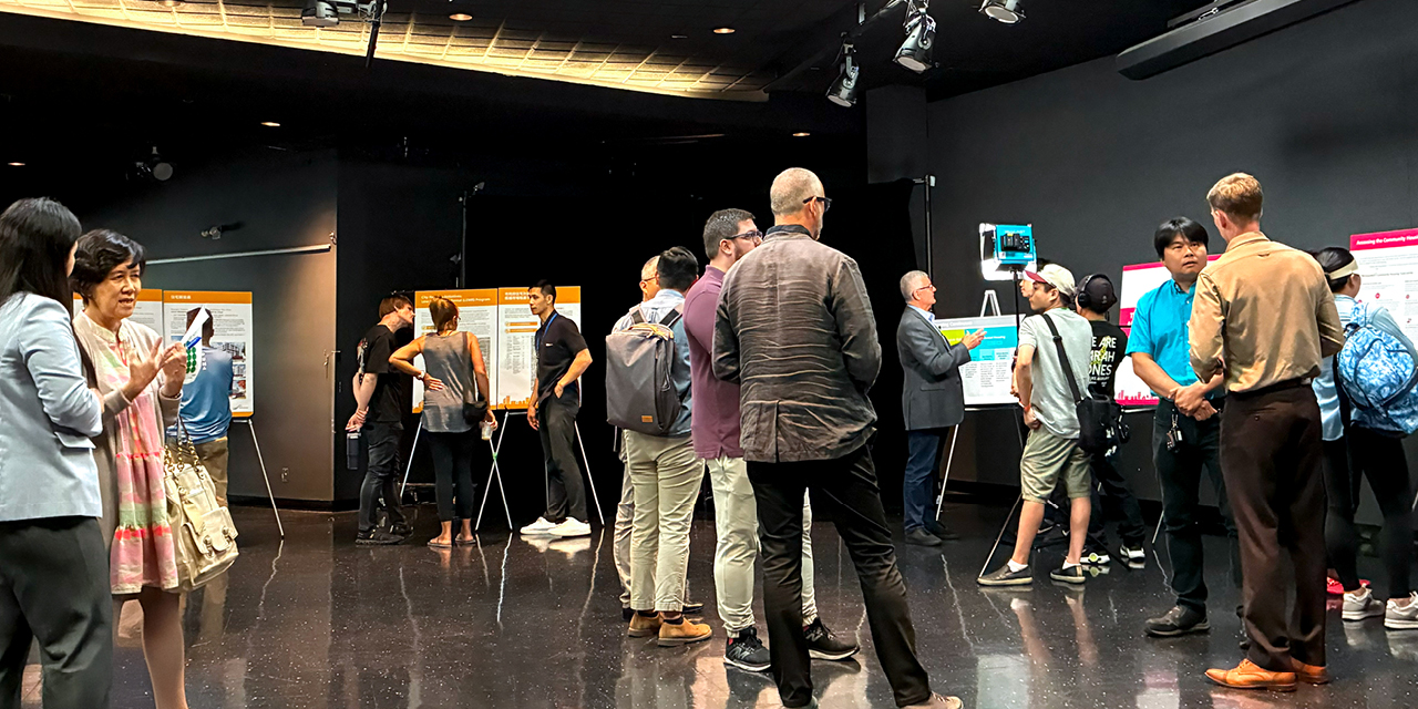 A wide angle shot of an indoor open house. Several people are standing talking to each other or looking at project display boards
