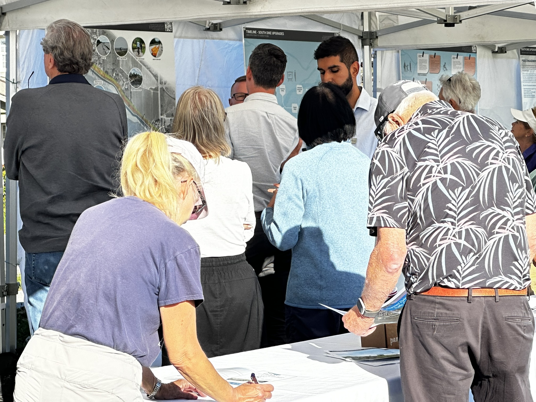 seven adult community members gathered around display boards at an open house