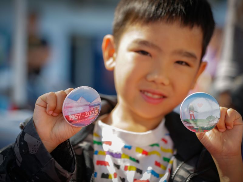 male child at a community event holding two custom buttons, one with a picture of the centre, the other with a picture of Sammie the Salmon
